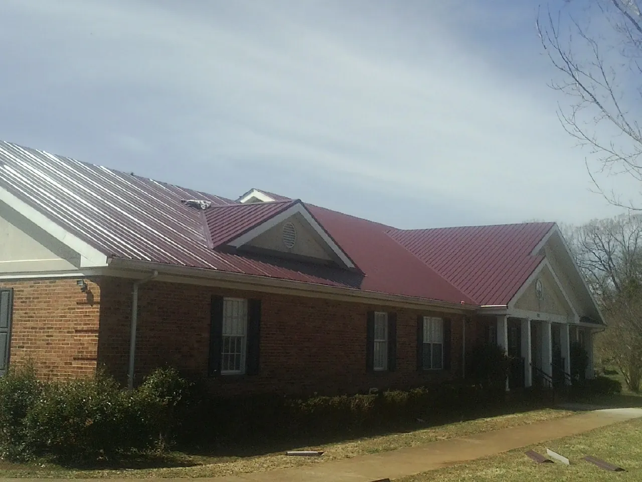 Red metal roof with gabled entries on a long brick building, from a Hail Damage Roof Repair job in Louvale