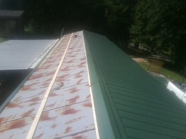 Old rusted panels beside newly installed green metal roofing — Wind Damage Roof Repair by Roofing Brothers in Louvale