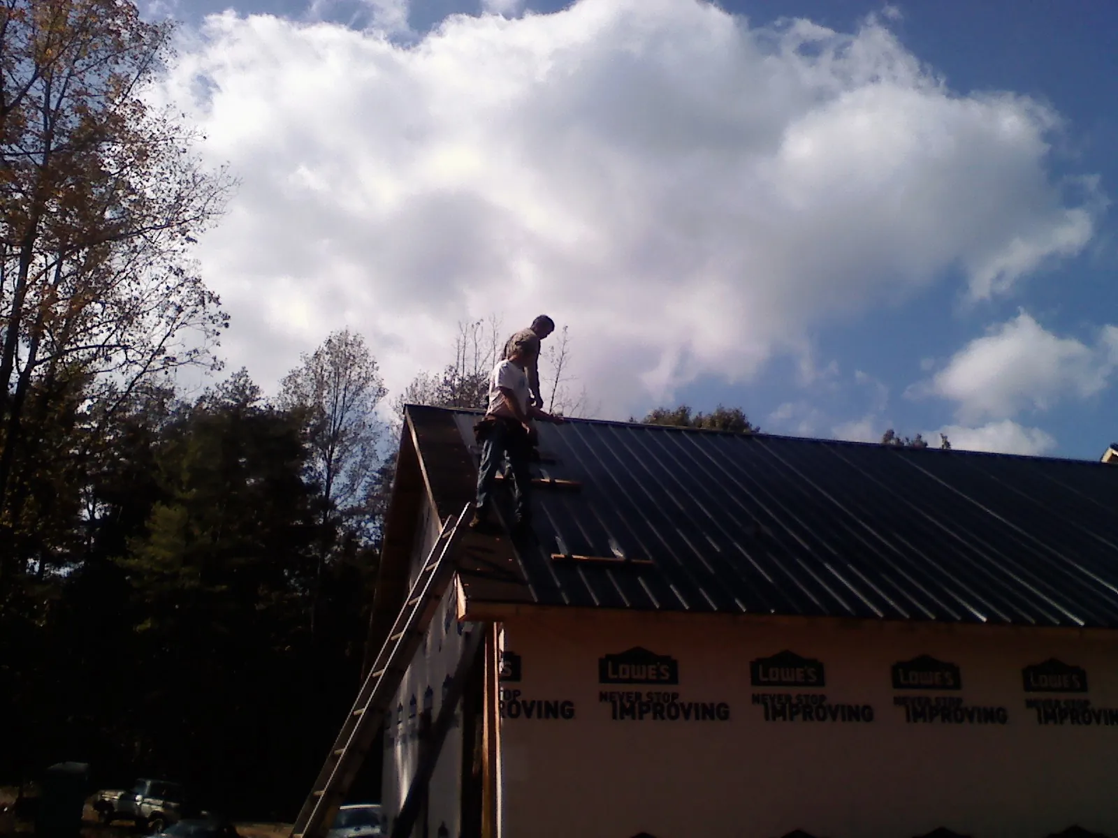 Roofer fastening dark metal panels high against a cloudy sky, from a Roof Inspection job in Louvale