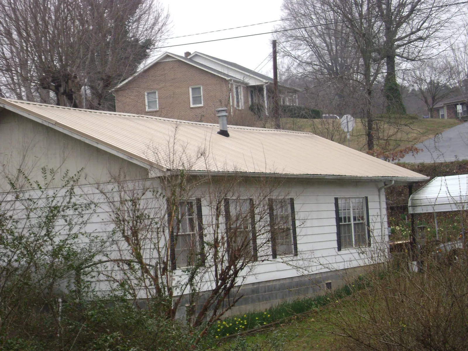 Tan metal roof on a white sided house set into a hillside — Commercial Roofing by Roofing Brothers in Louvale