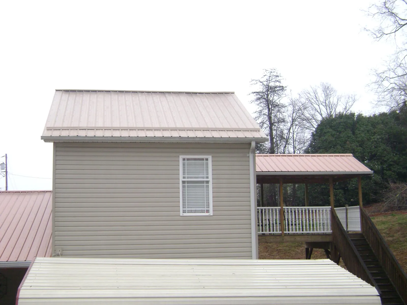 Tan metal roofs on a two story addition and attached porch, from a Roof Replacement job in Louvale